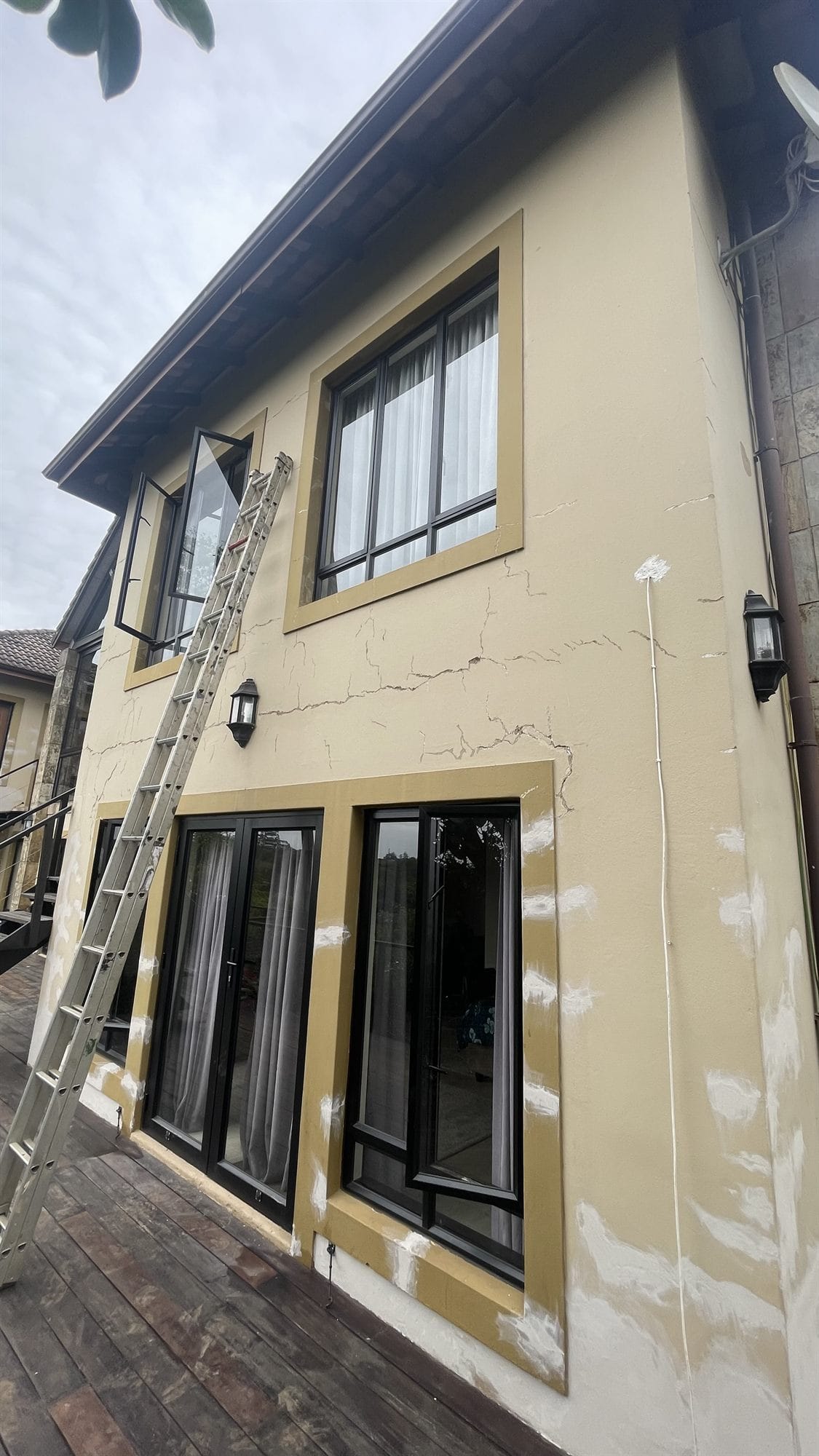 Estate home exterior before repainting - cracked render with filler patches and a ladder against the wall