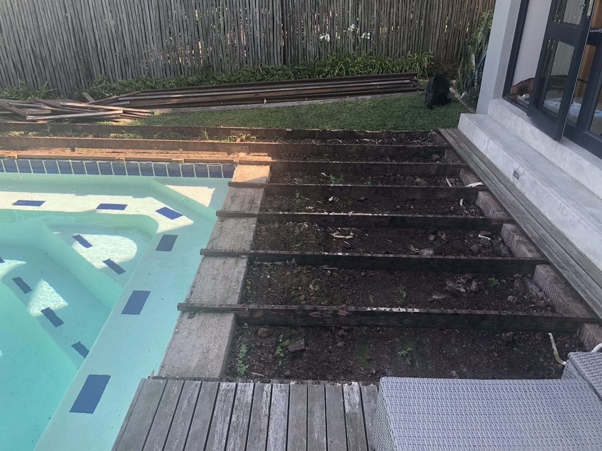 Pool deck before rebuilding - rotten boards lifted, exposing the joists underneath